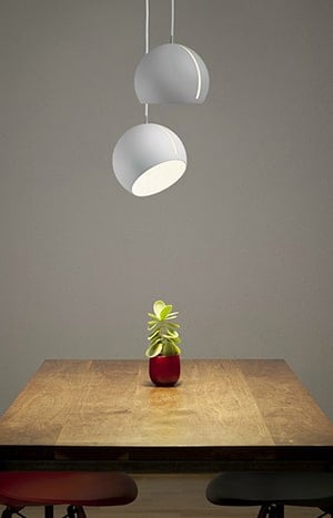 Moderne witte hanglamp boven eettafel met plant in rode pot.