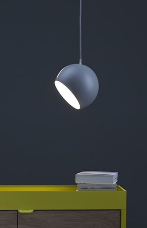 Strakke, moderne hanglamp boven een bureau met boeken.