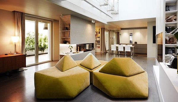 Moderne woonkamer met grote ramen, comfortabele groene stoelen en open keuken.