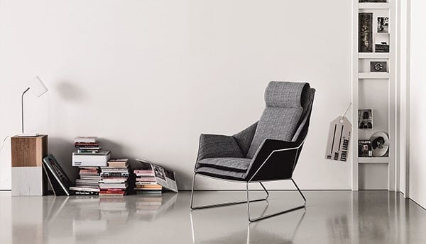 Minimalistische zithoek met grijze designstoel en boekenplank.
