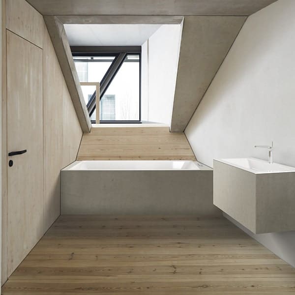 Minimalistische badkamer met bad en wastafel onder schuine dakramen.