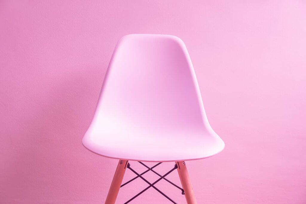 Moderne roze stoel met houten poten op roze achtergrond.