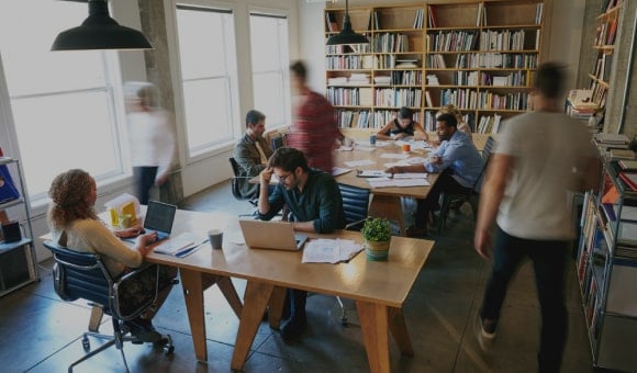 Diverse mensen werken samen in een moderne bibliotheek met boeken en laptops.